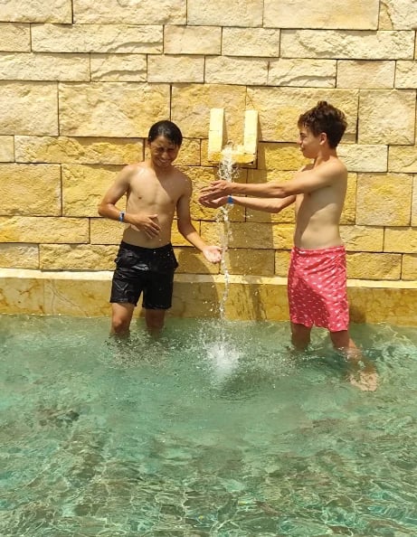 Dos niños jugando en agua turquesa pasándose una botella