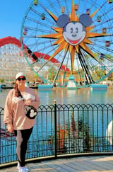 Woman posing at Disneys California Adventure Park with Mickey Mouse sun icon and Ferris wheel in background