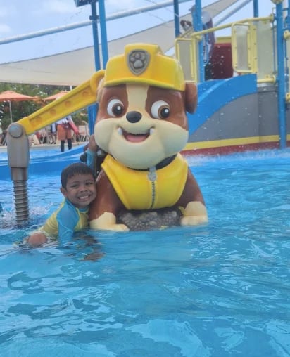 Niño nadando junto a un personaje de Paw Patrol en una piscina azul de parque acuático